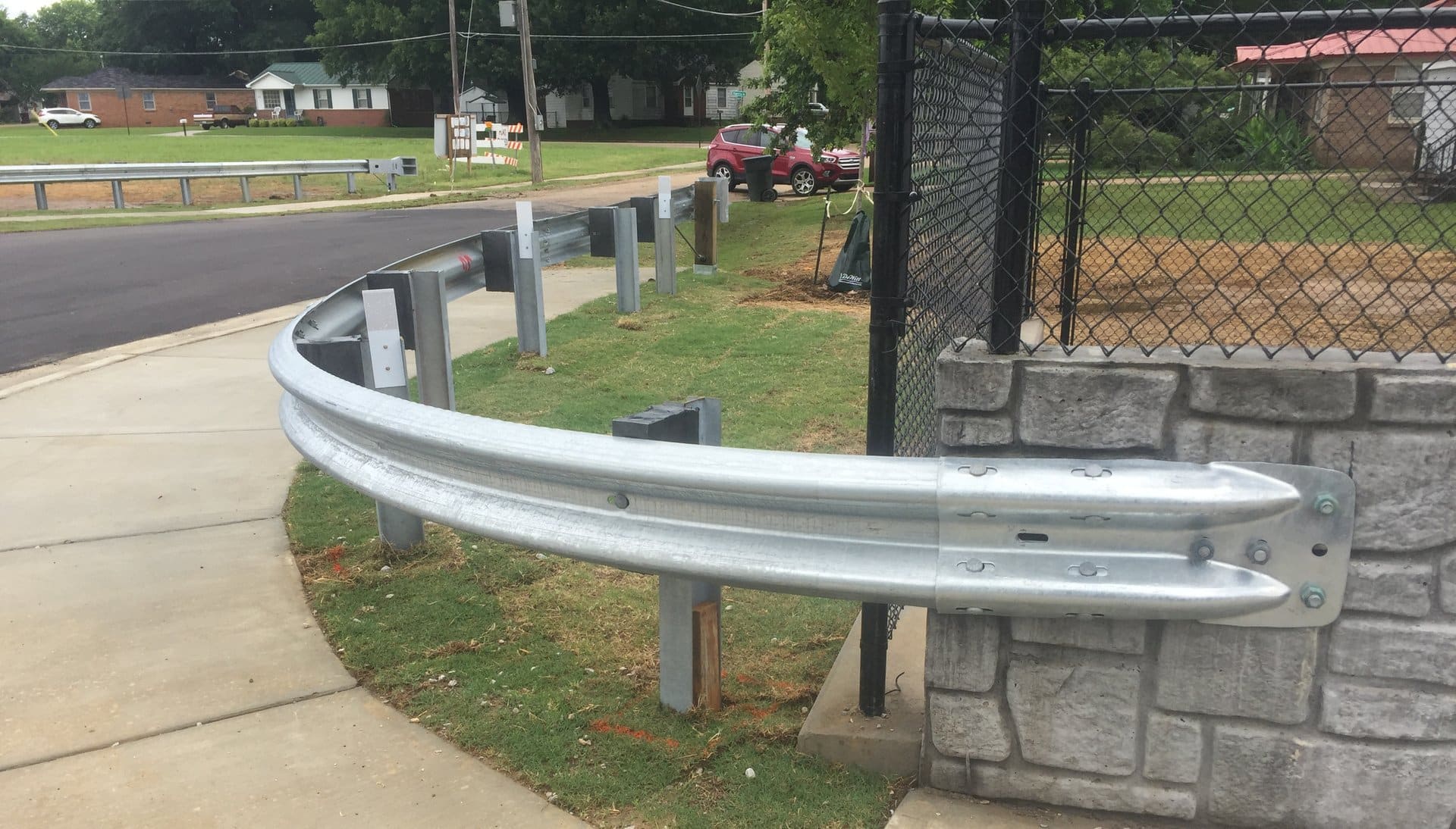 Curved radius guardrail wrapping a corner beside a chain-link fence